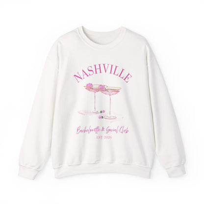 White crewneck sweatshirt with pink ‘Nashville’ bachelorette social club artwork featuring champagne coupe illustration, hand designed by Rebecca Illustrated