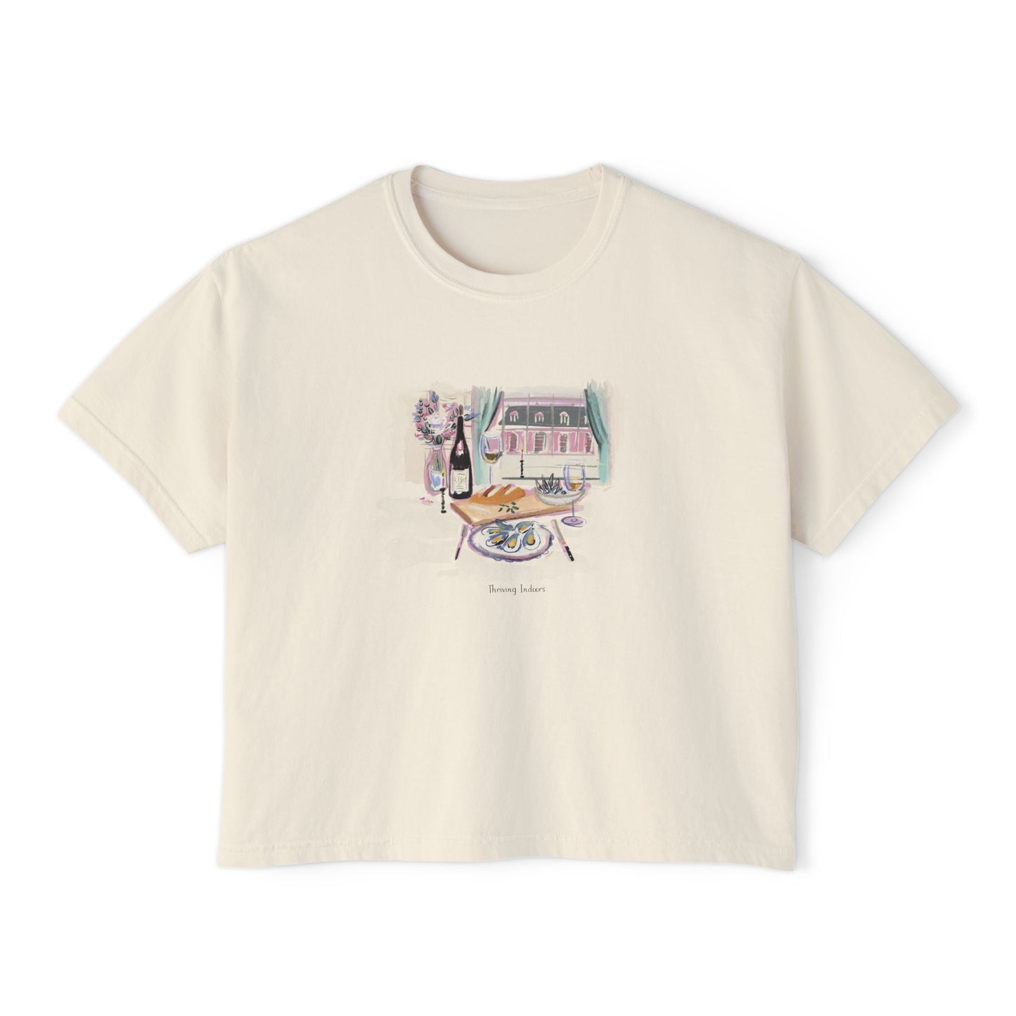 Cream cropped t-shirt featuring a hand-painted brunch scene with oysters, champagne, flowers, and a Parisian-style window view, with the text ‘Morning Indulge,’ illustrated by Rebecca Illustrated."