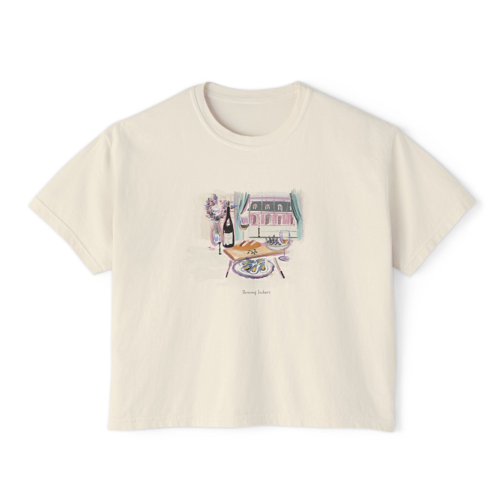 Cream cropped t-shirt featuring a hand-painted brunch scene with oysters, champagne, flowers, and a Parisian-style window view, with the text ‘Morning Indulge,’ illustrated by Rebecca Illustrated."