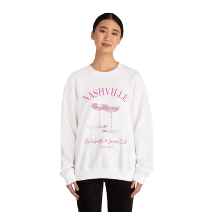 White crewneck sweatshirt with pink ‘Nashville’ bachelorette social club artwork featuring champagne coupe illustration, hand designed by Rebecca Illustrated