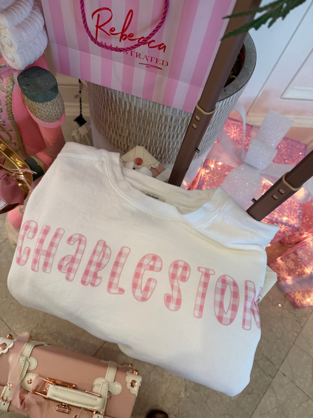 White crewneck sweatshirt with pink gingham ‘Charleston’ lettering across the chest, hand illustrated by Rebecca Illustrated.