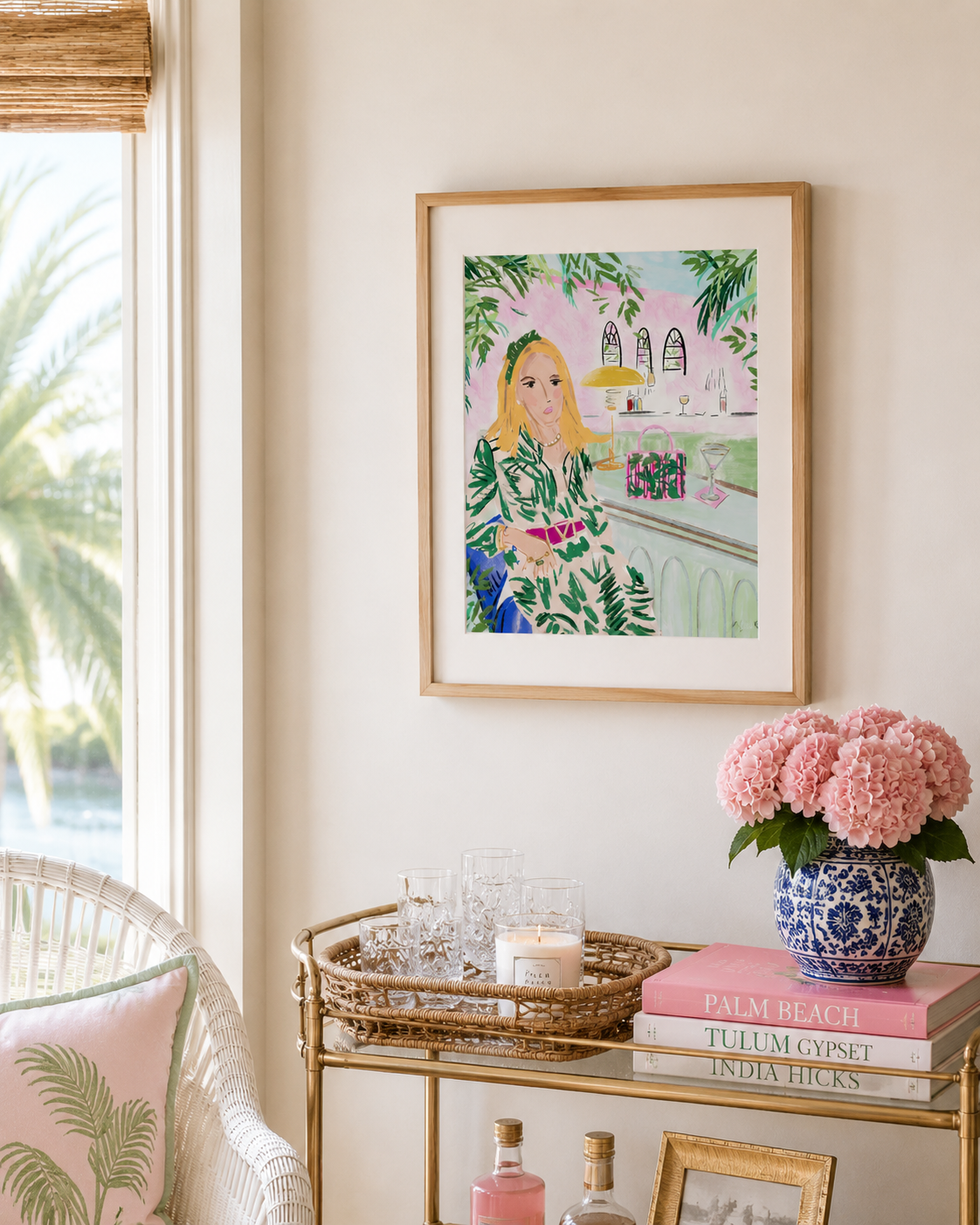 Framed artwork of a woman in a floral dress on a wall above a decorative table with pink flowers and books.