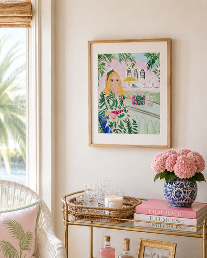 Framed artwork of a woman in a floral dress on a wall above a decorative table with pink flowers and books.