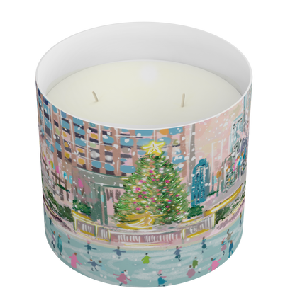 A cylindrical scented candle with a colorful winter city scene printed on the outside, filled with white wax and featuring two wicks, shown on a plain white background.