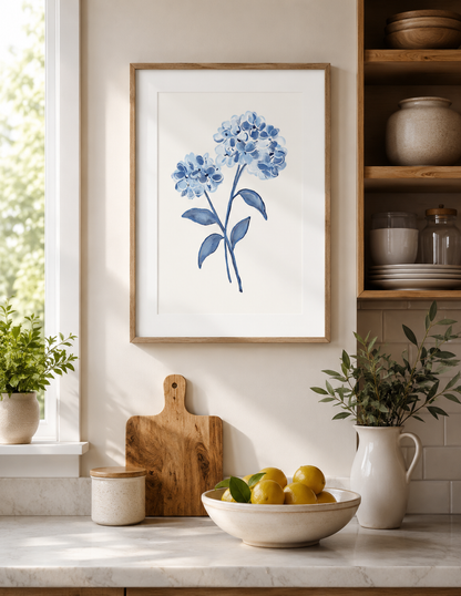 Kitchen interior with a framed blue flower print on the wall, cutting board, and bowl of fruit.