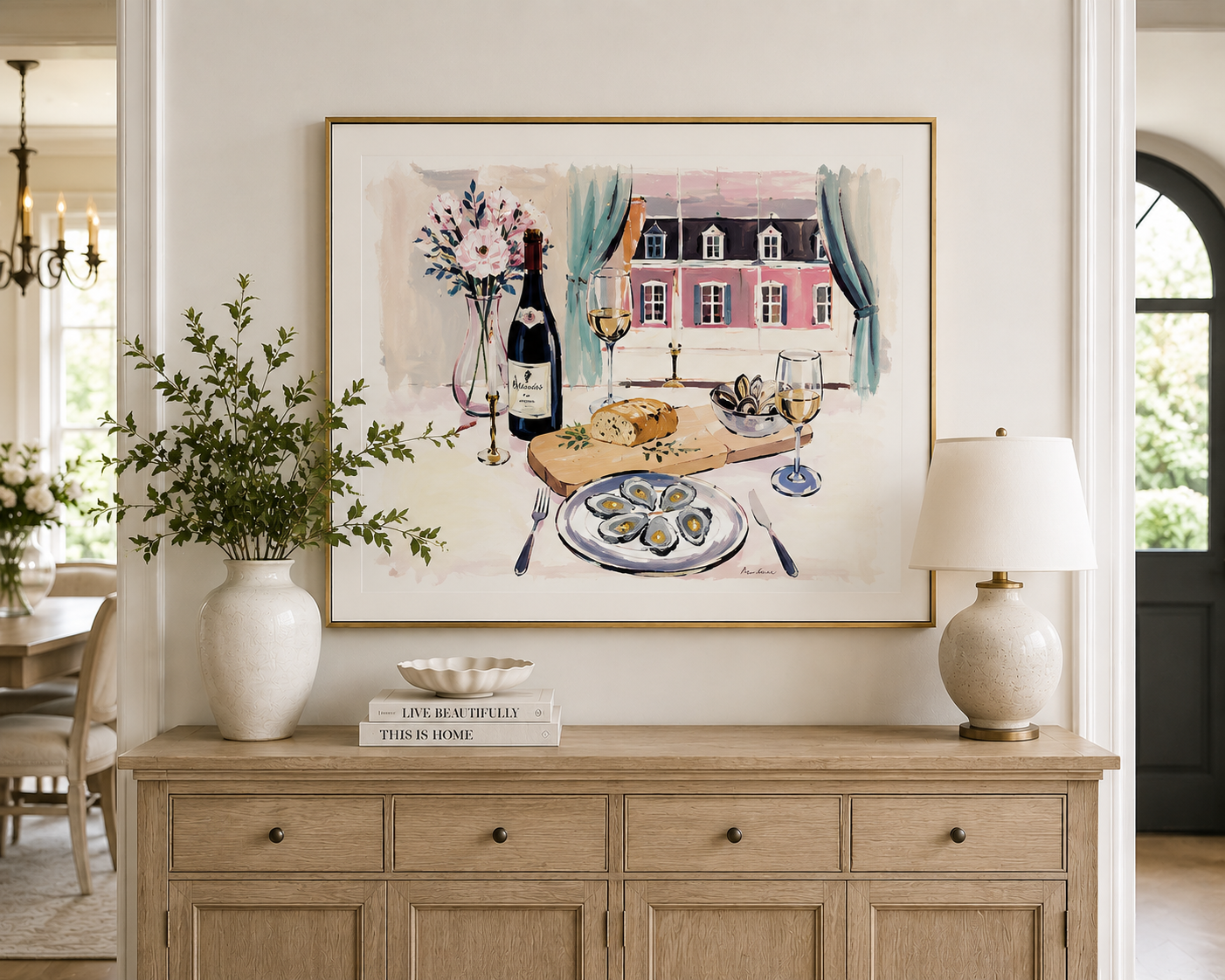 Watercolor-style painting by Rebecca Illustrated featuring oysters, a bottle of wine, and glasses of white wine on a dining table overlooking a pink French château through open blue curtains. Framed artwork displayed above a wooden sideboard in an elegant dining room.