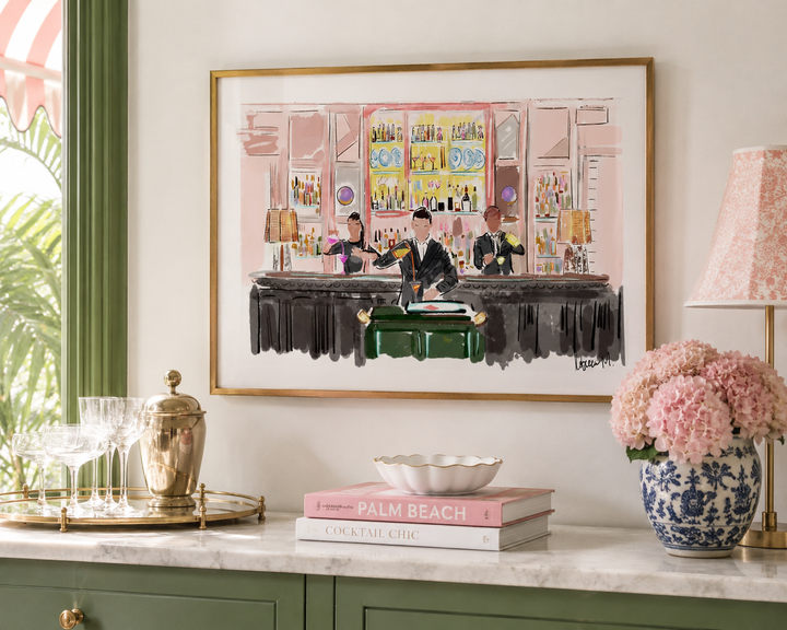 Framed artwork of a bar scene on a wall above a decorative table with books and a vase.