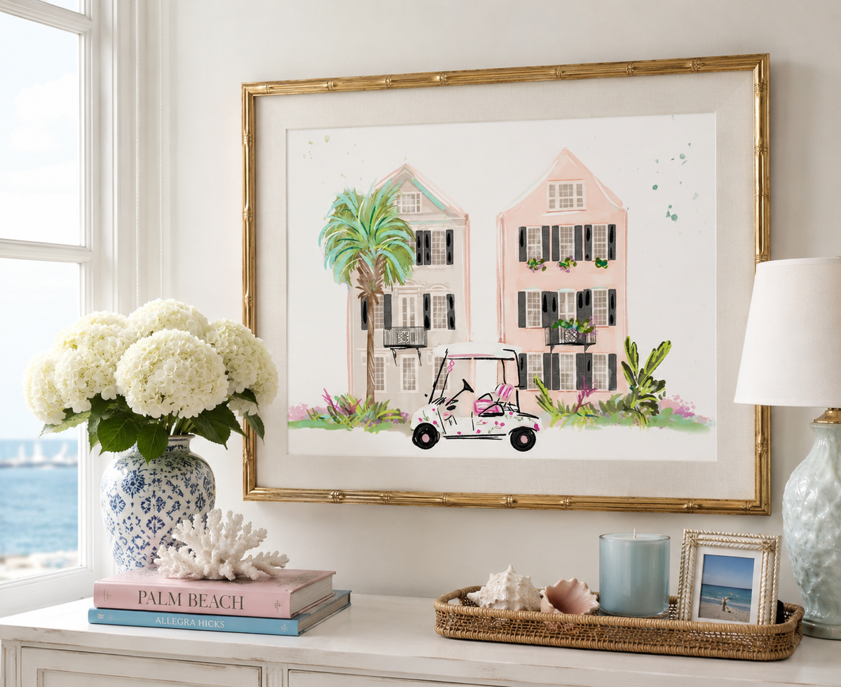 Framed artwork of a coastal scene with houses, palm trees, and a golf cart on a wall above decor items.