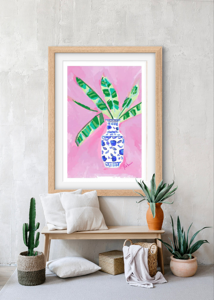 Watercolor-style illustration of green banana leaves in a blue-and-white vase against a bright pink background.