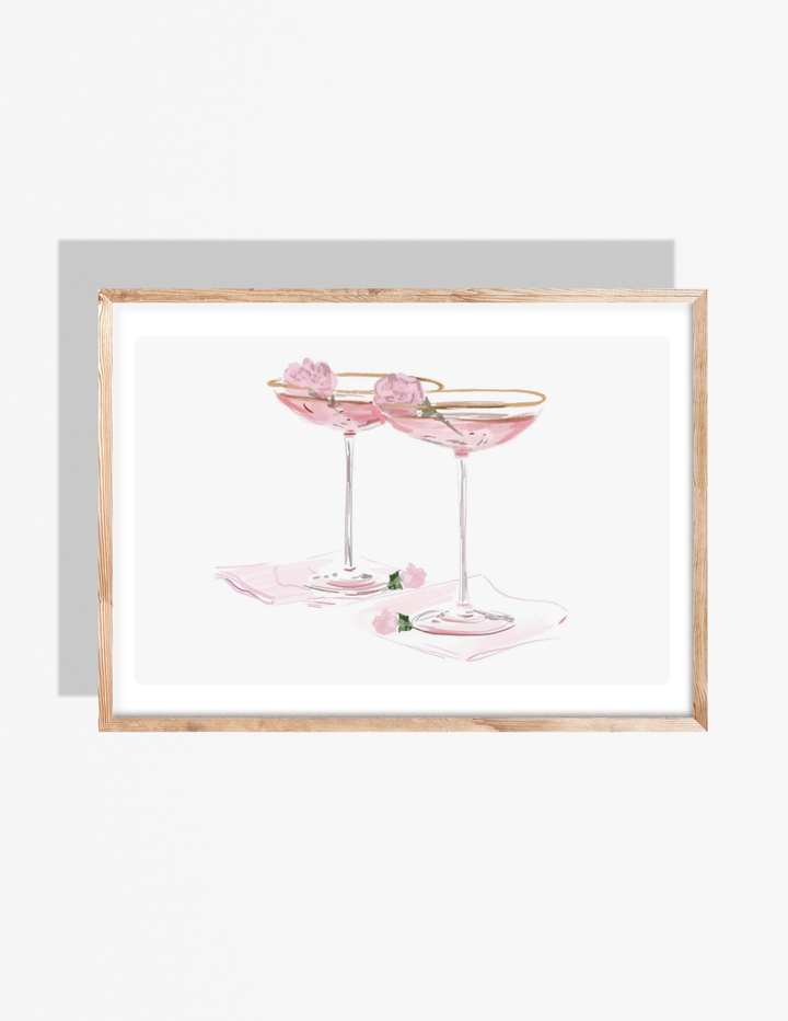 A soft pastel illustration by Rebecca Illustrated of two pink champagne coupe glasses with gold rims, each garnished with a small pink flower, resting on light pink napkins.
