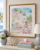 Framed artwork of a woman in a pink dress with palm trees and a cityscape, displayed on a shelf with decorative items.