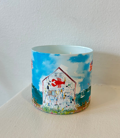 Rebecca Illustrated candle featuring a coastal lobster shack adorned with a red lobster sign, nautical fishing gear, sailboats, and waterfront scenery against a bright blue sky.