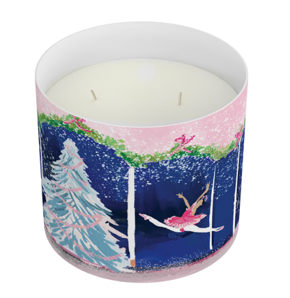 A two wick scented candle in a white cylindrical container with a winter-themed wraparound illustration featuring a ballerina, a Christmas tree, and snow in pink, blue, green, and white.