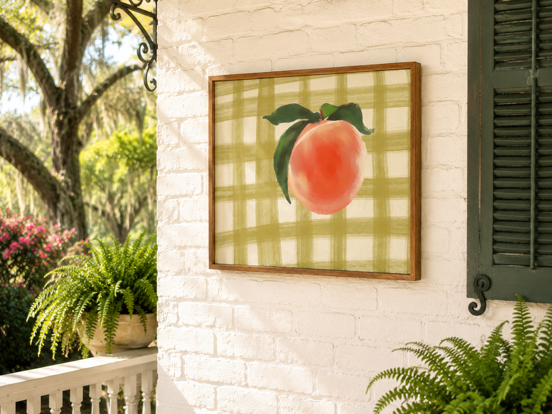 Framed artwork of a peach on a white brick wall with greenery