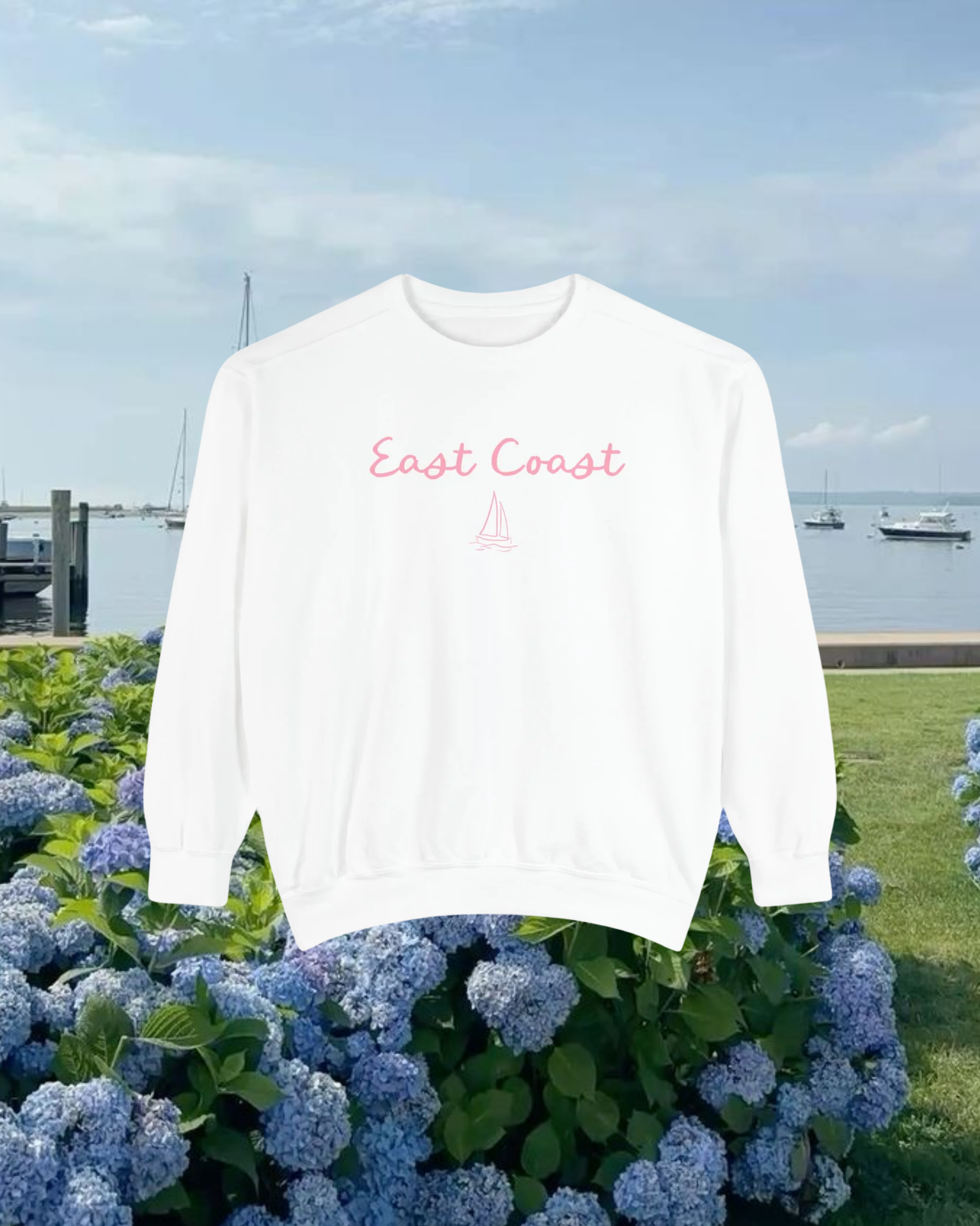 White sweatshirt with 'East Coast' text on a background of blue hydrangeas and a dock.