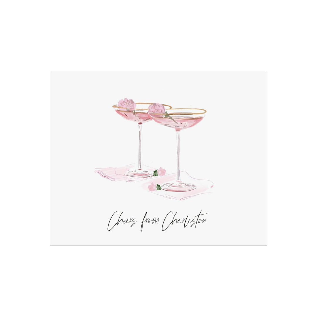 Illustration of two pink coupe cocktails with gold rims and flower garnishes on napkins, with text ‘Cheers from Charleston,’ artwork by Rebecca Illustrated.