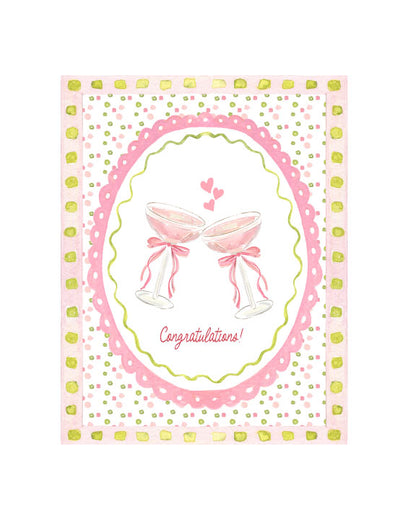 Illustrated congratulations greeting card featuring two pink cocktail glasses with bows, hearts, and a decorative pink patterned border, by Rebecca Illustrated.