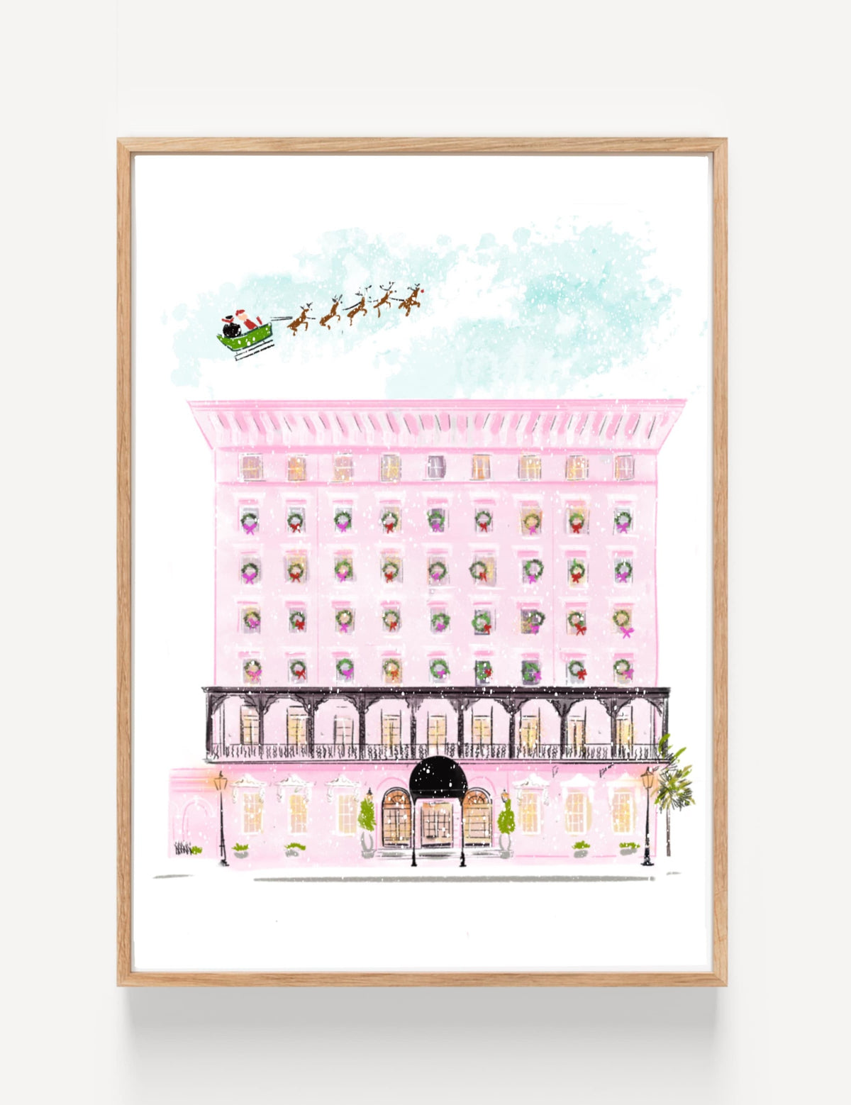 Christmas art print of a pink hotel decorated with wreaths, with Santa and his reindeer flying overhead, illustrated by Rebecca Illustrated.